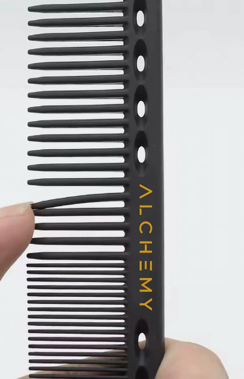 A hand holding the Alchemy Master Cutting Comb, with its gold branding visible
